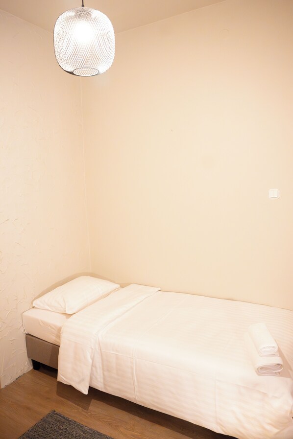 A single bed with white bedding and a rolled towel, a textured hanging light fixture, and a wooden floor. - Hotelik Relax H360 (Lódz)
