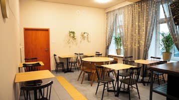 A dining area with multiple tables and chairs, a wooden door, and potted plants.