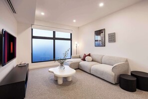 Een moderne woonkamer met een groot raam, een bank, een salontafel en een televisie.