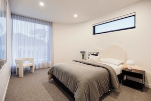 A bedroom with a bed, a nightstand, a chair, and a window with curtains.
