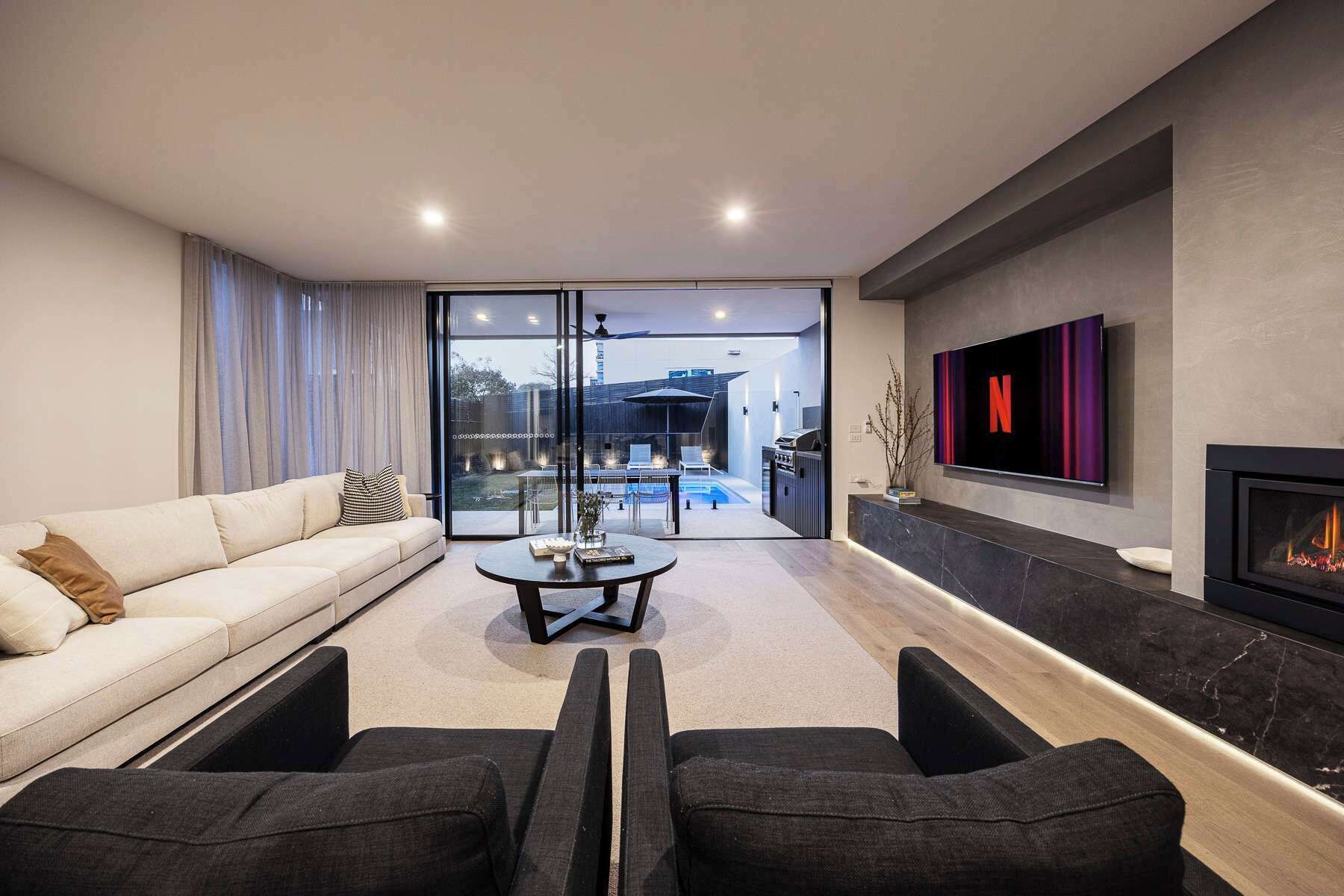 A modern living room with a sofa, two armchairs, a coffee table, a fireplace, and a TV mounted on the wall.