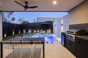 An outdoor patio area with a pool, a barbecue grill, and a dining table with chairs.