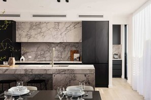 Een moderne keuken met marmeren aanrechtbladen, een centraal eiland met zitplaatsen, en een eethoek voor zes personen.