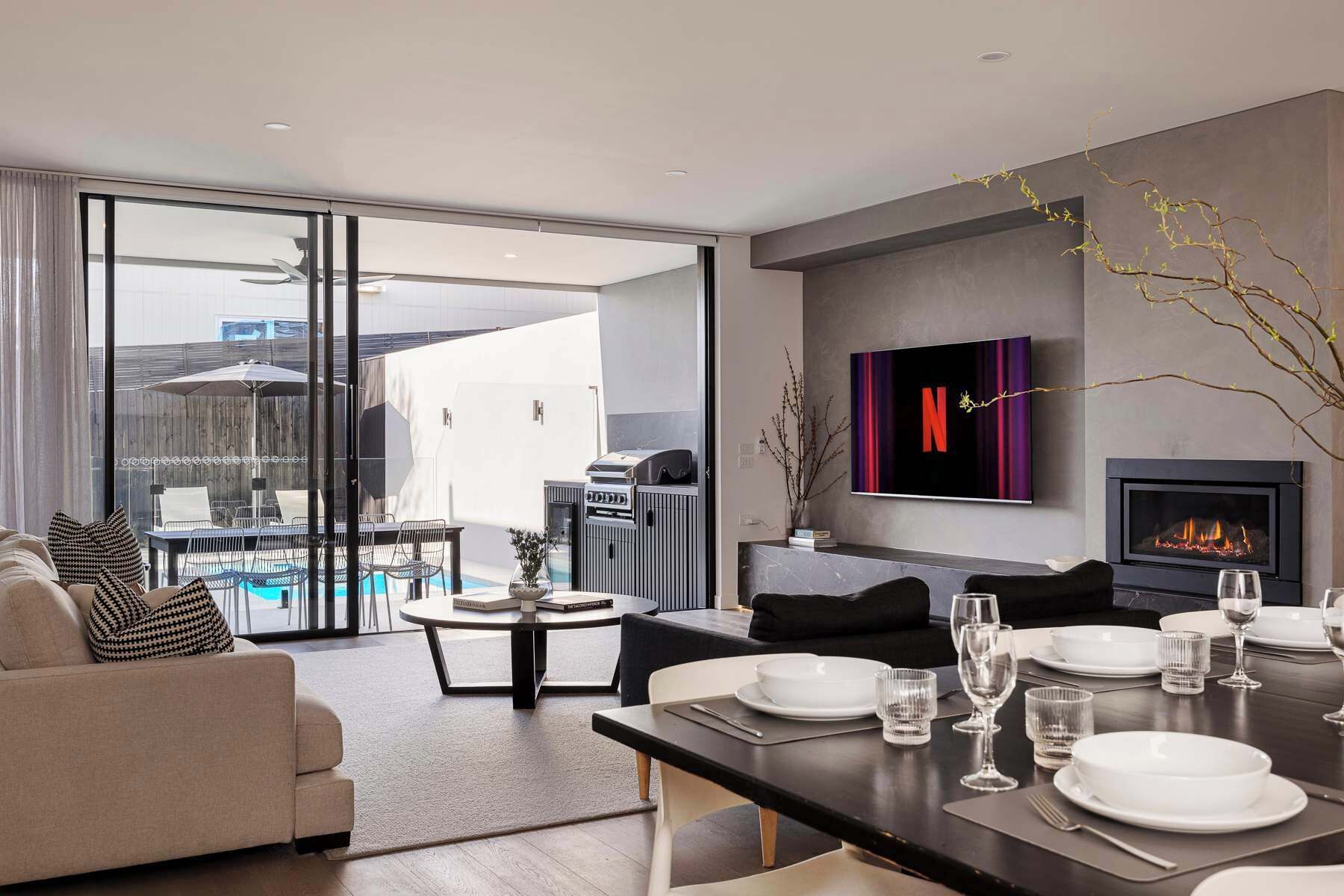 A modern living room with a dining area, a fireplace, and a TV mounted on the wall.
