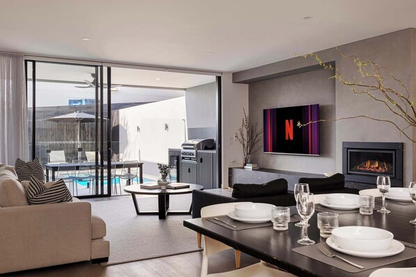 A modern living room with a dining area, a fireplace, and a TV mounted on the wall.