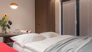 Una camera da letto con un letto, un comodino con un vaso di fiori, una sedia rossa e una finestra con persiane.