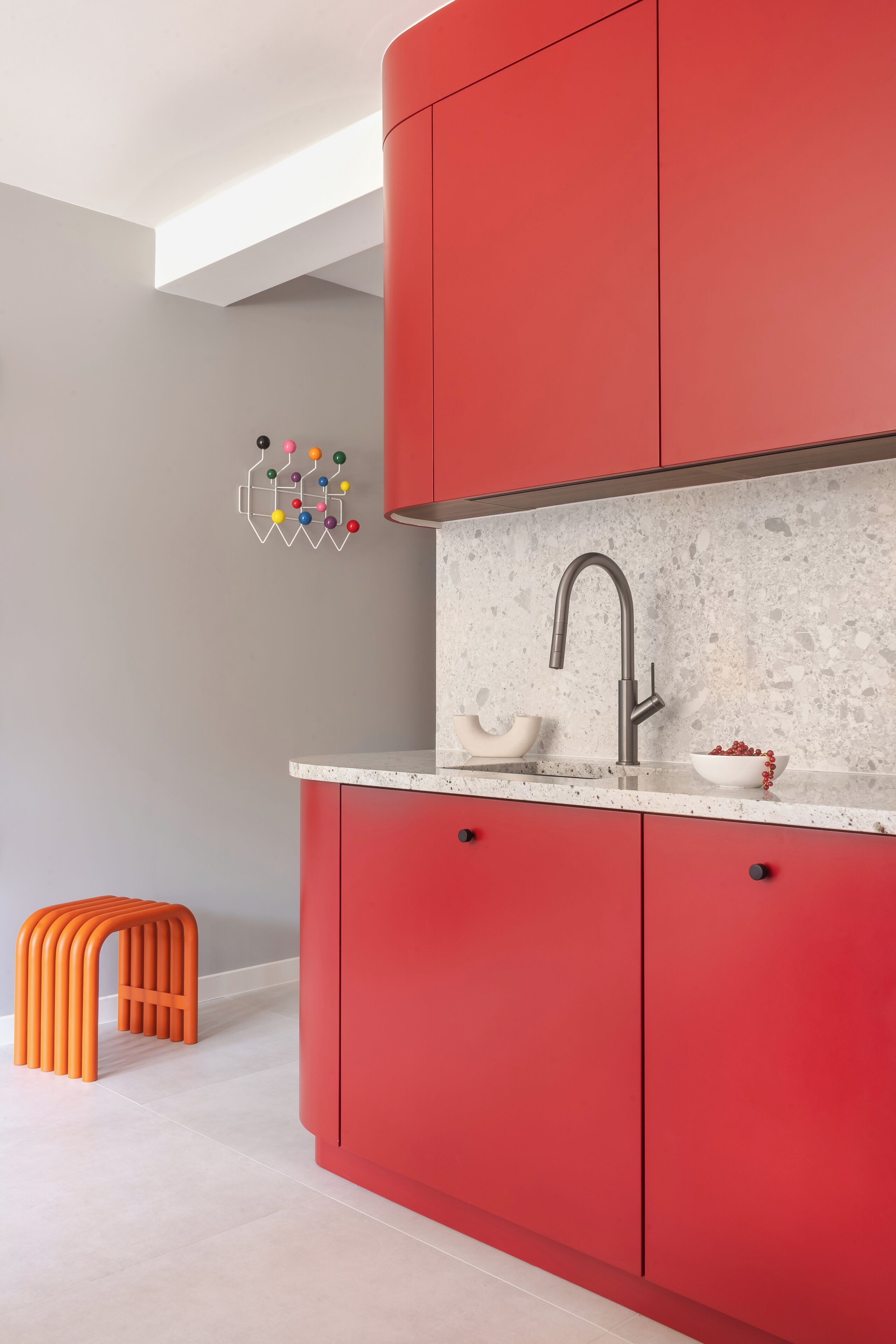 A modern kitchen with red cabinets, a granite countertop, and a stainless steel faucet.