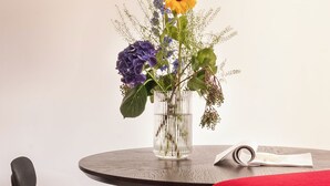 Un tavolo rotondo con un vaso trasparente pieno di fiori, una sedia nera e un divano rosso.