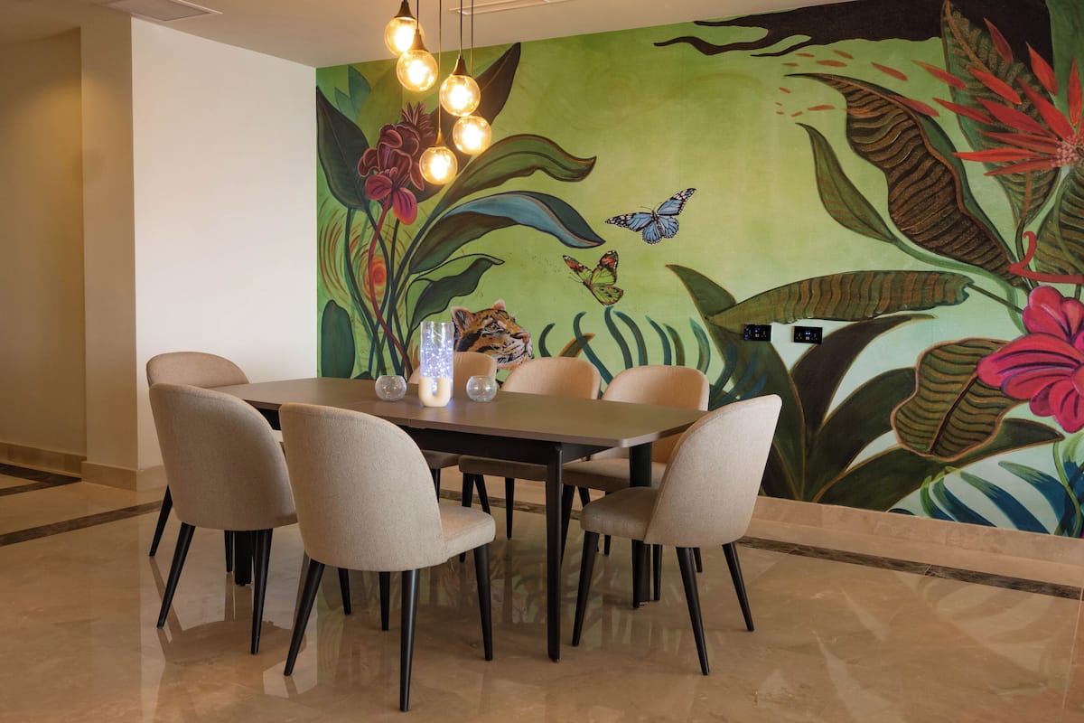 Un área de comedor con una mesa y sillas, un mural con diseños florales y de mariposas en la pared, y un candelabro.