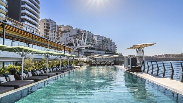 A rooftop pool with lounge chairs and umbrellas, overlooking a cityscape. - Best View Fortina Luxury Suites  (Sliema)