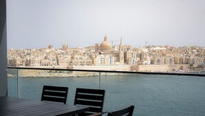 A balcony with a table and chairs overlooking a cityscape with historic buildings and a waterfront. - Best View Fortina Luxury Suites  (Sliema)