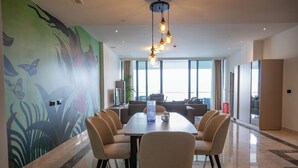 A modern dining area with a long table, six chairs, and a decorative light fixture. - Best View Fortina Luxury Suites  (Sliema)