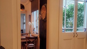 A room with a wooden floor, a sofa, a dining area with chairs and a table, and a large window with a view of greenery. - Annette's Place, Greenwich (London) - Garden Apartment (close to the O2 Arena) (London)