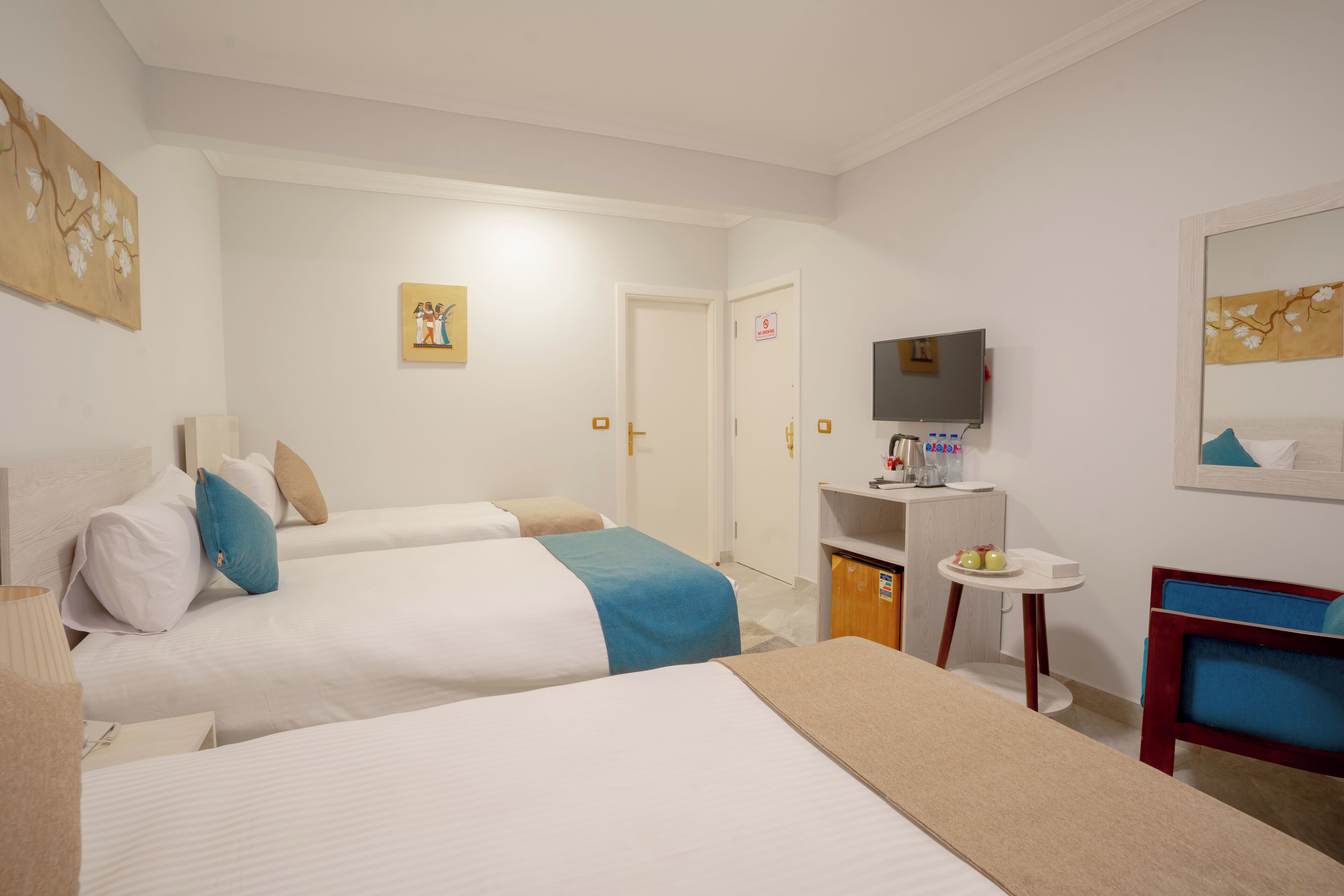 A hotel room with two beds, a desk, a chair, a television, and artwork on the walls.