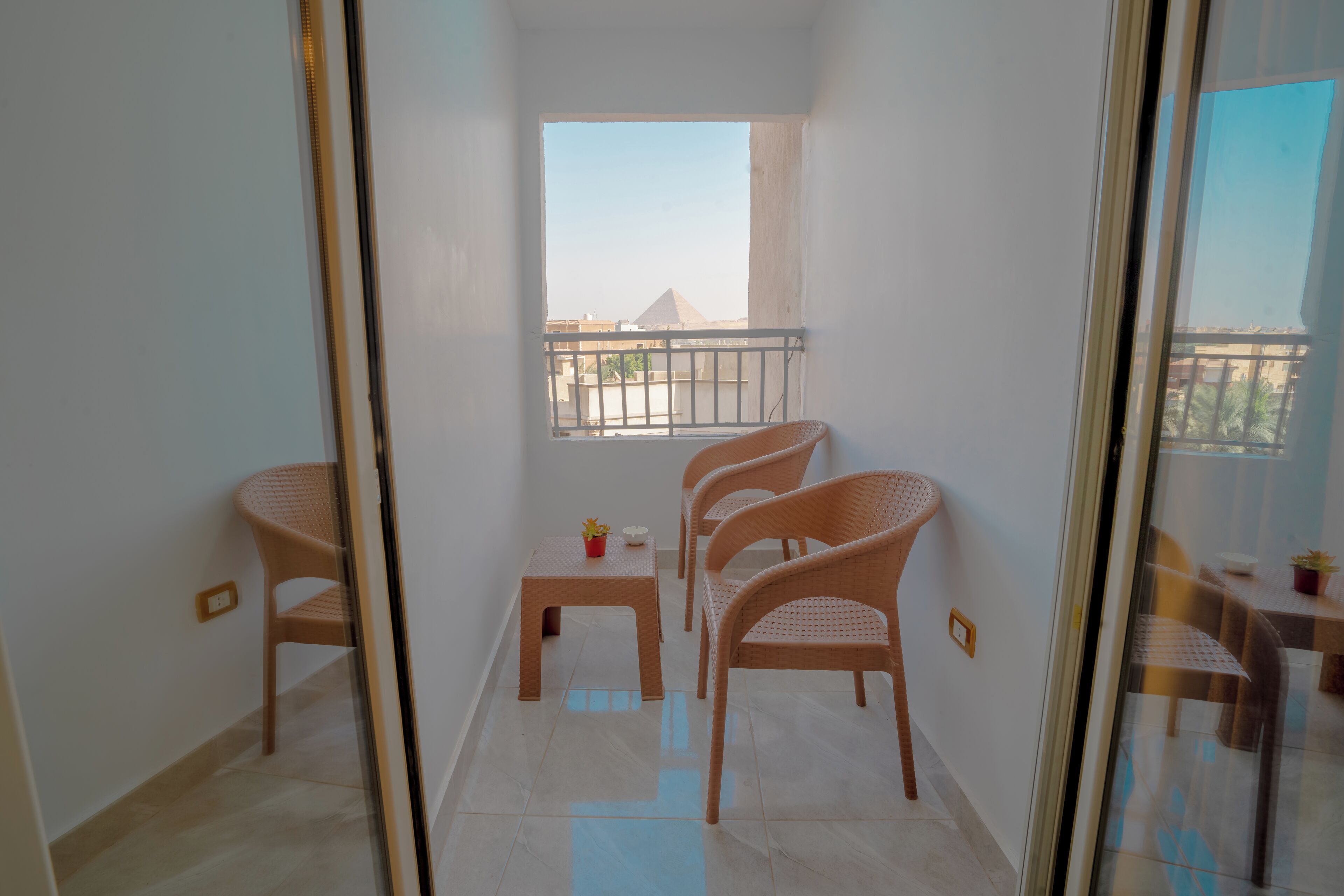 A balcony with a view of buildings, a small table with a potted plant, and wicker chairs.