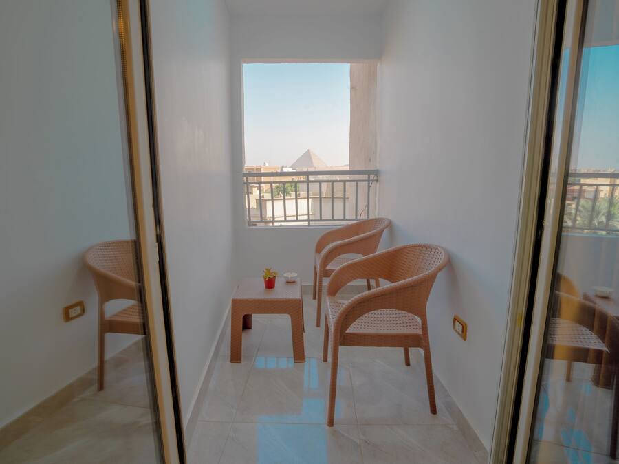 A balcony with a view of buildings, a small table with a potted plant, and wicker chairs.