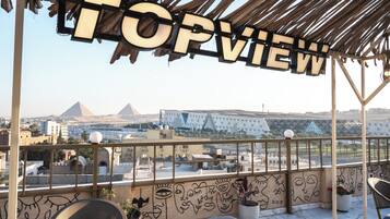 Una terraza en la azotea con vistas a pirámides, un edificio moderno y un letrero que dice 'TOPVIEW'.