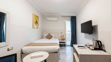 Una habitación de hotel con una cama, un escritorio con hervidor, un televisor y una ventana con cortinas.