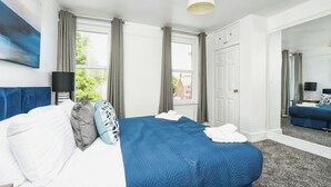 A hotel room with a large bed, a flat-screen TV, a window with curtains, a door, and a mirror.