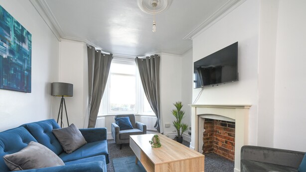 A modern living room with a blue sofa, a wooden coffee table, a fireplace, and a flat-screen TV mounted on the wall.