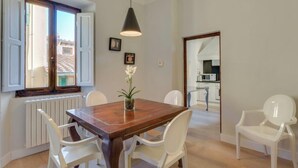 A dining area with a wooden table and white chairs, a hanging light fixture, and a view of the kitchen through an open door. - Stunning Holiday Apartment in the Heart of Florence (Firenze)