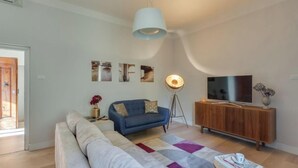 A modern living room with a sofa, a blue armchair, a floor lamp, a TV on a wooden cabinet, and a large window. - Stunning Holiday Apartment in the Heart of Florence (Firenze)