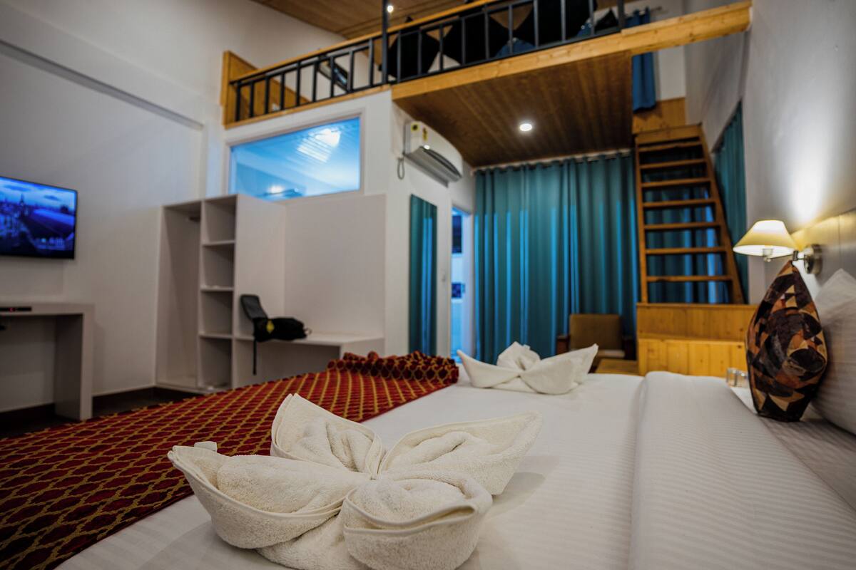 A hotel room with a bed, a TV, a desk, and a staircase.