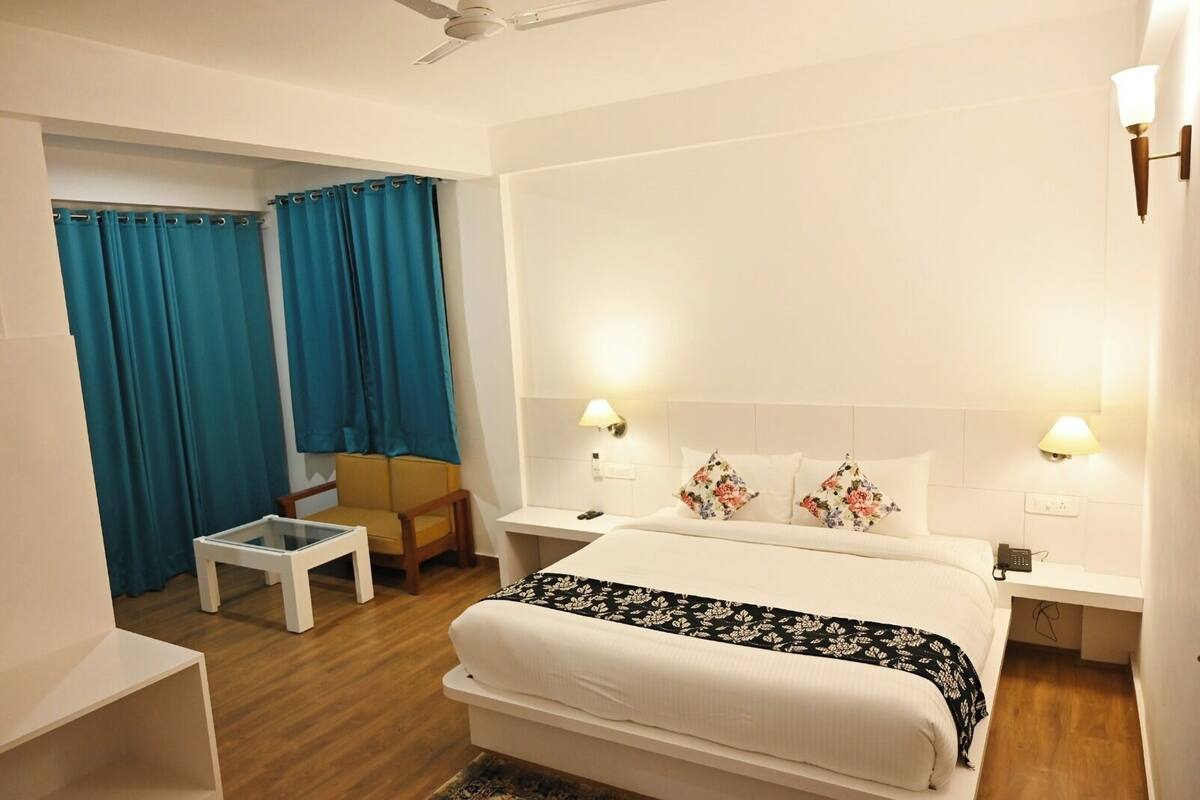 A hotel room with a bed, two bedside lamps, a chair, a small table, and a ceiling fan.