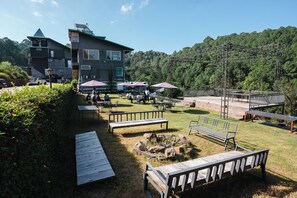 An outdoor patio area with picnic tables, benches, and umbrellas, surrounded by a forested hillside.