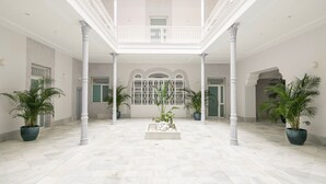 Amplio espacio interior con techo alto, columnas blancas y una jardinera central con rocas y plantas.