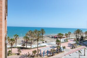 Une vue sur la plage, avec des palmiers, un lido et une route menant à un parking.