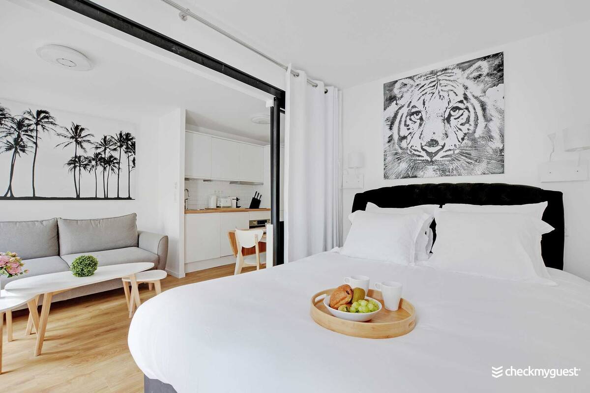 Une chambre d’hôtel moderne dotée d’un grand lit, d’un coin repas et d’une cuisine visible à travers une porte ouverte.