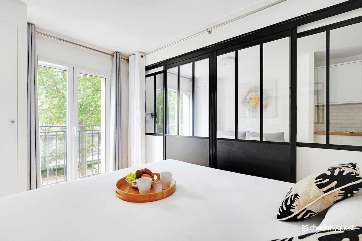 Une chambre d’hôtel avec un grand lit, un plateau en bois contenant des articles pour le petit-déjeuner, une vue sur la verdure et une fenêtre à cadre noir.