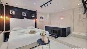 A modern hotel room with a large bed, a small seating area, a bathtub, and a shower. - Résidence Paris Rochechouart (Paris)