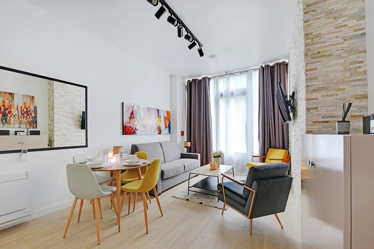 A modern living room with a dining area, featuring a sofa, chairs, a coffee table, and artwork on the walls.