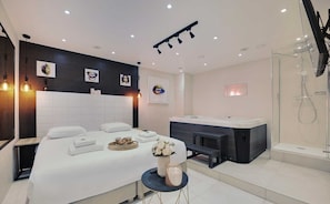 A modern hotel room with a large bed, a small seating area, a bathtub, and a shower. - Résidence Paris Rochechouart (Paris)
