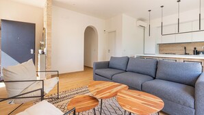 A modern living room with a grey sofa, a coffee table, and a chair. There is a kitchen area with a white countertop and a wooden backsplash. - 4147 Villa Daversa by Barbarhouse (Manduria)