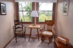 A traditional room with a wooden chair, table, and lamp, set against a large window.