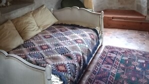 A bedroom with a bed, a rug, a window with curtains, and a stone wall. - Château-l'evêque en Périgord (Château-l'Évêque)