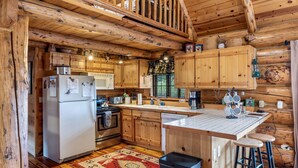 Un rustico chalet in legno con una cucina dotata di mobili in legno, frigorifero, fornello e lavello.