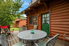 Een houten chalet met een ronde tafel en stoelen, een groene deur en een overdekt terras.