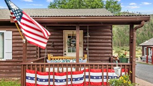 A wooden cabin with a porch, an American flag, and a Texas state flag. - Cottage Room on Main (Greer)