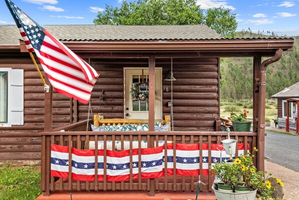 A wooden cabin with a porch, an American flag, and a Texas state flag. - Cottage Room on Main (Greer)