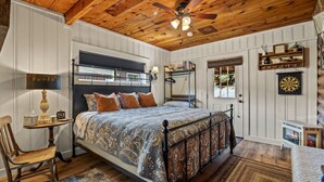 A bedroom with a large bed, a ceiling fan, a bedside table with a lamp, a chair, and a small table with decorative items. - Cottage Room on Main (Greer)