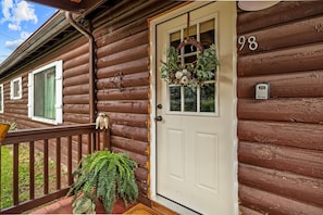 A wooden cabin with a white door, a number '98, and a wreath on the door. - Cottage Room on Main (Greer)