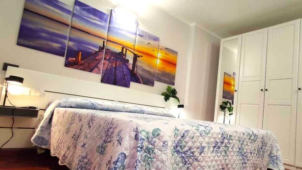 Um quarto com cama, mesa de cabeceira, luminária, guarda-roupa e uma parede com três quadros.