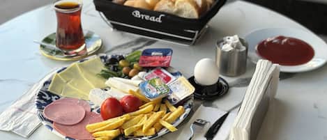 A table with a variety of food items including bread, a plate with ham, cheese, and tomatoes, a glass of tea, and condiments.