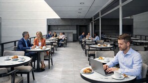 Un moderno café al aire libre con mesas y sillas redondas, algunas con portátiles y pasteles.