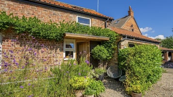 A brick house with a tiled roof, a wooden porch, and a gravel driveway.