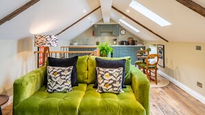 A cozy loft apartment with a green sofa, wooden beams, a kitchen area, and a dining table. - Haxby Hayloft: A Charming Countryside Retreat Near York (York)